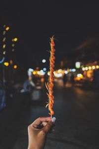 Close-up of cropped hand holding prawns on skewer against illuminated lights at night