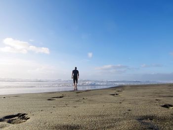 Rear view of man walking on shore at beach against sky