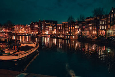 Illuminated buildings by river against sky at night