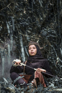 Portrait of young woman sitting on land in forest