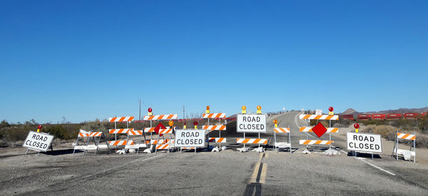 Signboards with barricade on road against clear blue sky