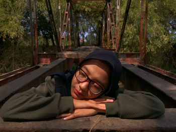 Close-up of young woman relaxing on metallic structure against trees