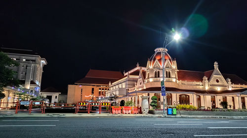 Illuminated building by street against sky at night