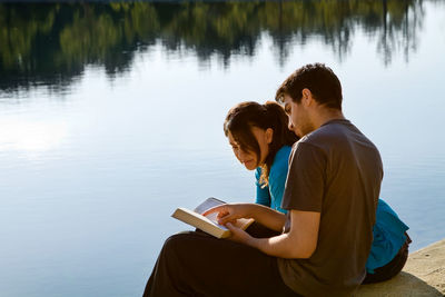 Rear view of man using mobile phone while sitting on lake