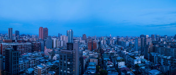 Aerial view of buildings in city against blue sky