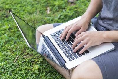 Midsection of woman using laptop while sitting on grassy field