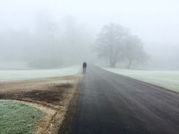 Young man standing on road in forest during foggy weather