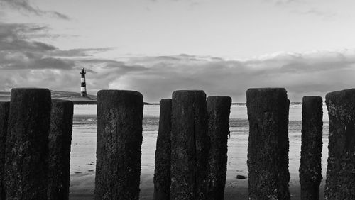 Wooden posts in sea against sky