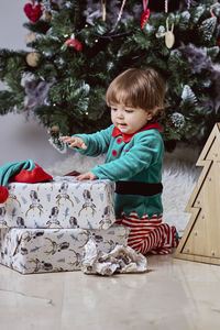 A little 12-month-old christmas elf with a christmas tree and gifts