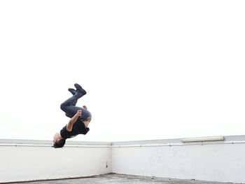 Side view of man backflipping on building terrace against sky