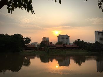 Scenic view of lake by buildings against sky during sunset