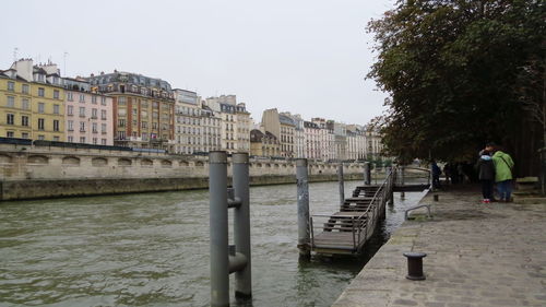 Man by river in city against clear sky