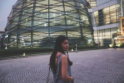 Side view of young woman standing against building in city