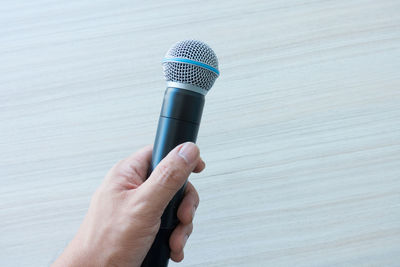 Cropped hand holding microphone against wall