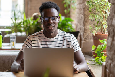 Smiling man using laptop while sitting in cafe