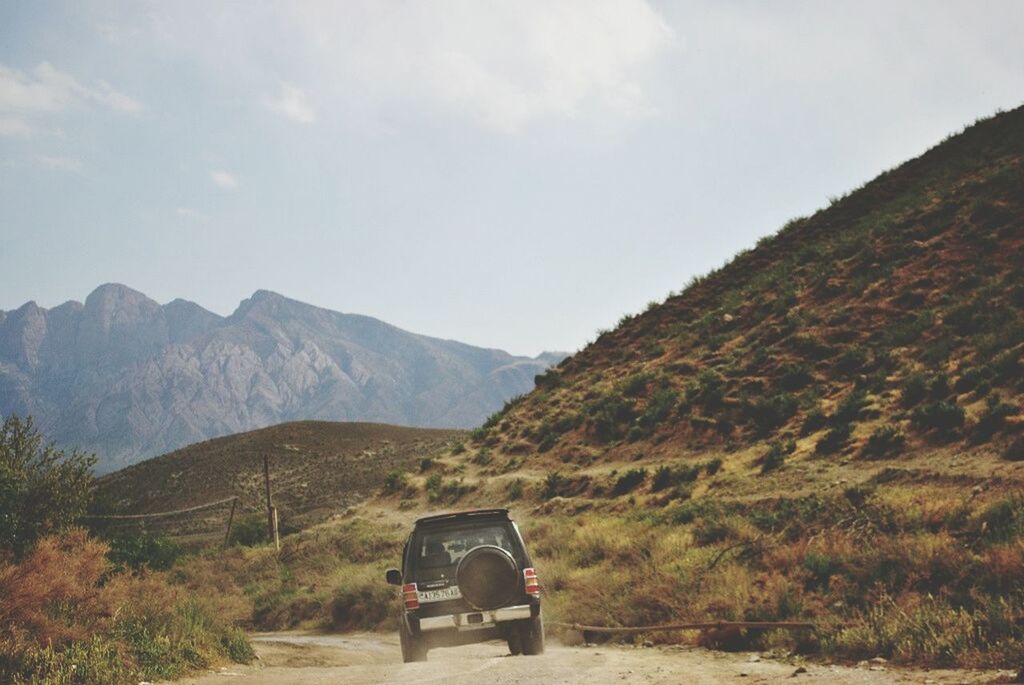 VEHICLE ON DIRT ROAD BY MOUNTAINS