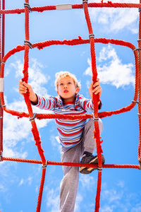 Low angle view of boy on monkey bar in playground against sky