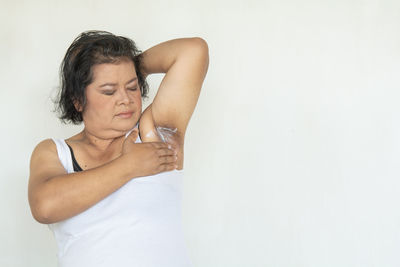 Midsection of woman holding glass while standing against white background