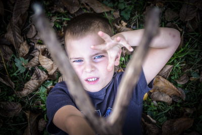 High angle portrait of boy holding stick while lying on field