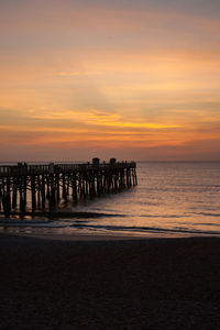 Silhouette wooden posts on beach against sky during sunset