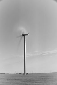 Wind turbines on field by sea against sky