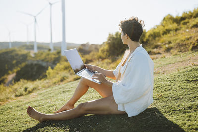 Woman holding laptop while sitting on mountain