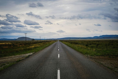 Empty road amidst field against sky