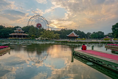 Ferris wheel by lake against cloudy sky during sunset