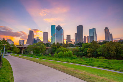 Road by buildings against sky during sunset