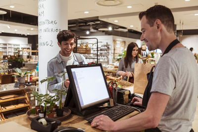 Cashier using computer while talking to smiling customer at checkout counter