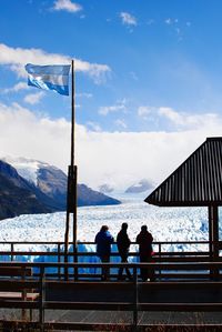 Rear view of people at observation point by icebergs against sky