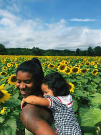 Mother piggybacking daughter while standing amidst sunflowers
