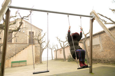 Young girl sheltered in an abandoned swing set with hood, unrecognisable.