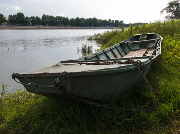 Boat moored on field by lake against sky