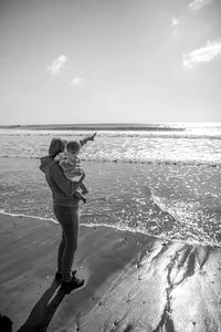 Rear view of friends standing at beach against sky