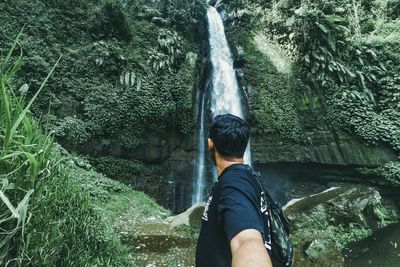 Woman standing on rock against waterfall in forest