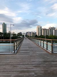 Footbridge over footpath amidst buildings in city against sky