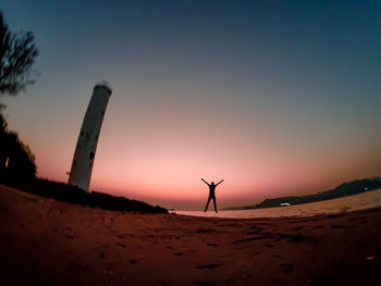 Silhouette woman on sand at beach against sky during sunset