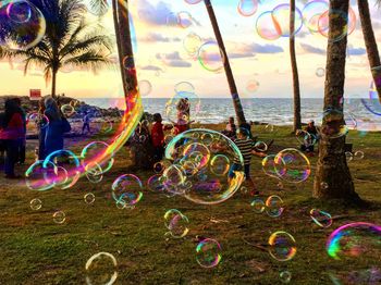 Bubbles in mid-air with people at beach during sunset