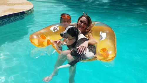 High angle portrait of mother with daughter and dog swimming in pool