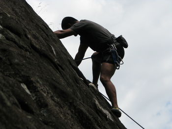 Low angle view of man climbing on rock against sky