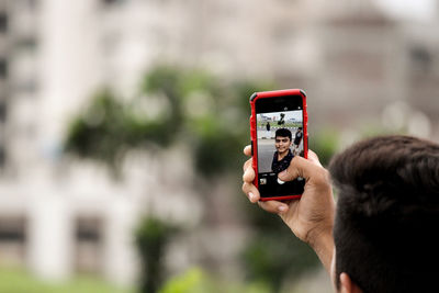Cropped image of man taking selfie through mobile phone on street