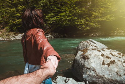 Cropped hand of man holding girlfriend hand at riverbank in forest