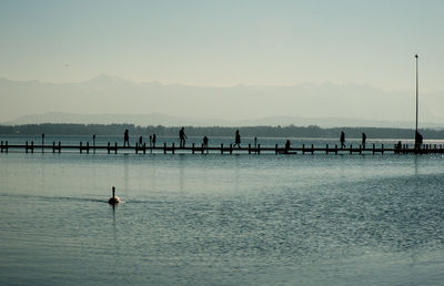 Silhouette people on sea against clear sky