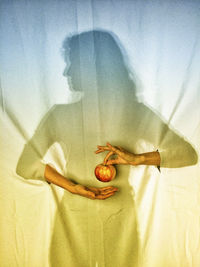 Woman with hands coming out and holding apple while standing against curtain