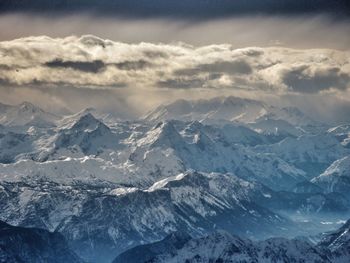 Scenic view of snow covered mountain range with cloudy sky