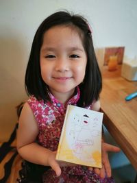 Portrait of smiling girl holding book at table
