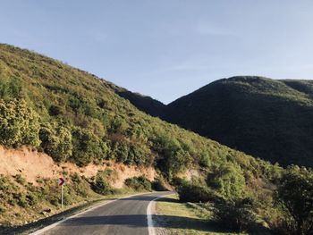 Country road by mountains against sky