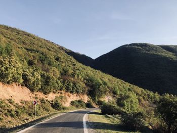 Country road by mountains against sky