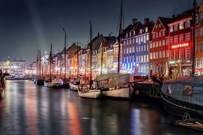 Boats moored in canal by buildings against sky at night